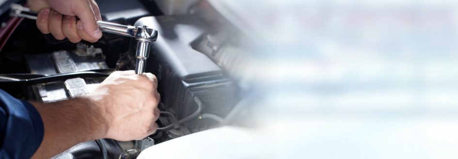 Close-up of a man's hand holding tools over a car engine