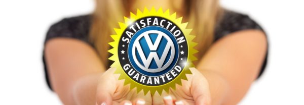 A girl holding out a badge with "VW" in the center and "Satisfaction Guaranteed" around it referencing the extended Volkswagen warranty